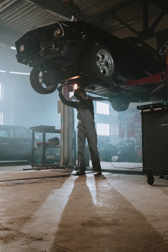 Mastering the First Impression: Your intriguing post title goes here Mechanic performing maintenance on elevated car in dimly lit garage, showcasing automotive repair work.