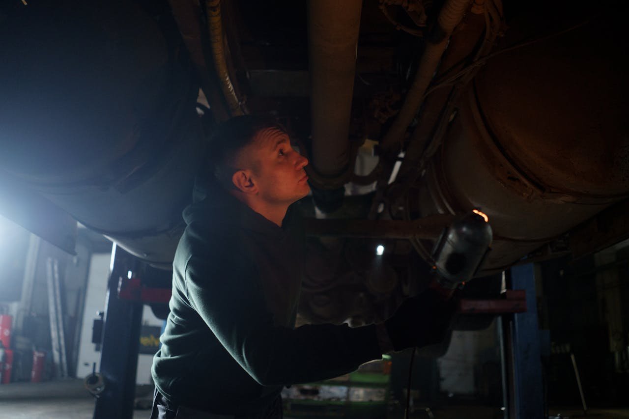 The Art of Drawing Readers In: Your attractive post title goes here Auto mechanic inspects vehicle underbody in a garage setting with dim lighting.